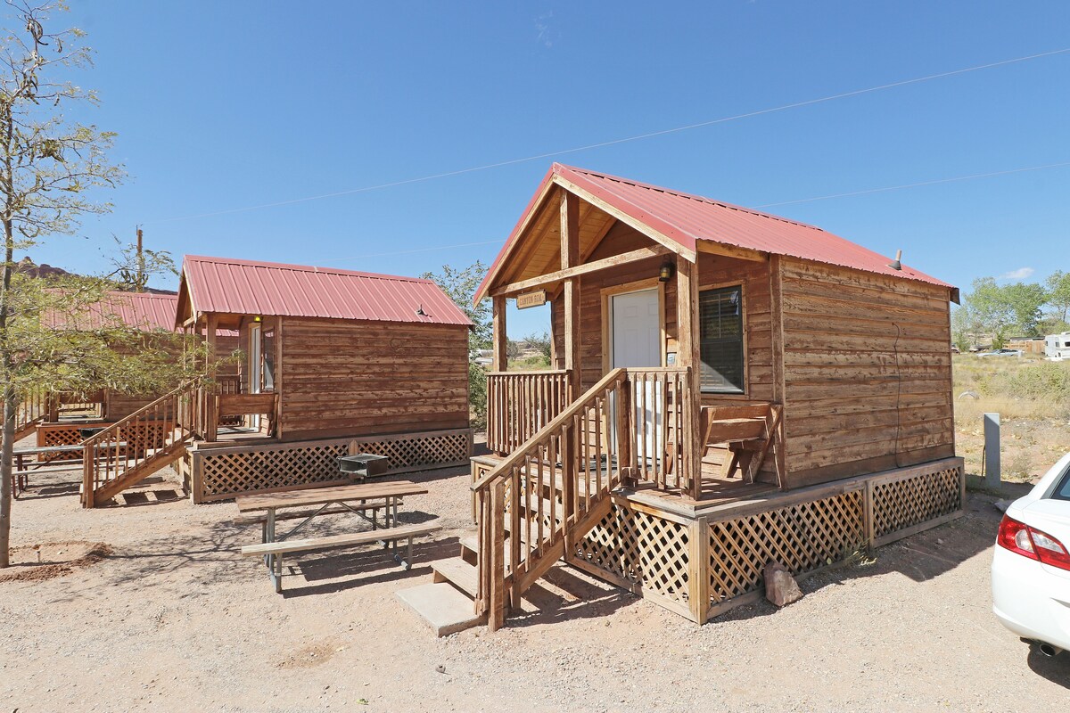 Two wooden cabins with red roofs, wooden decks, and a covered picnic table.