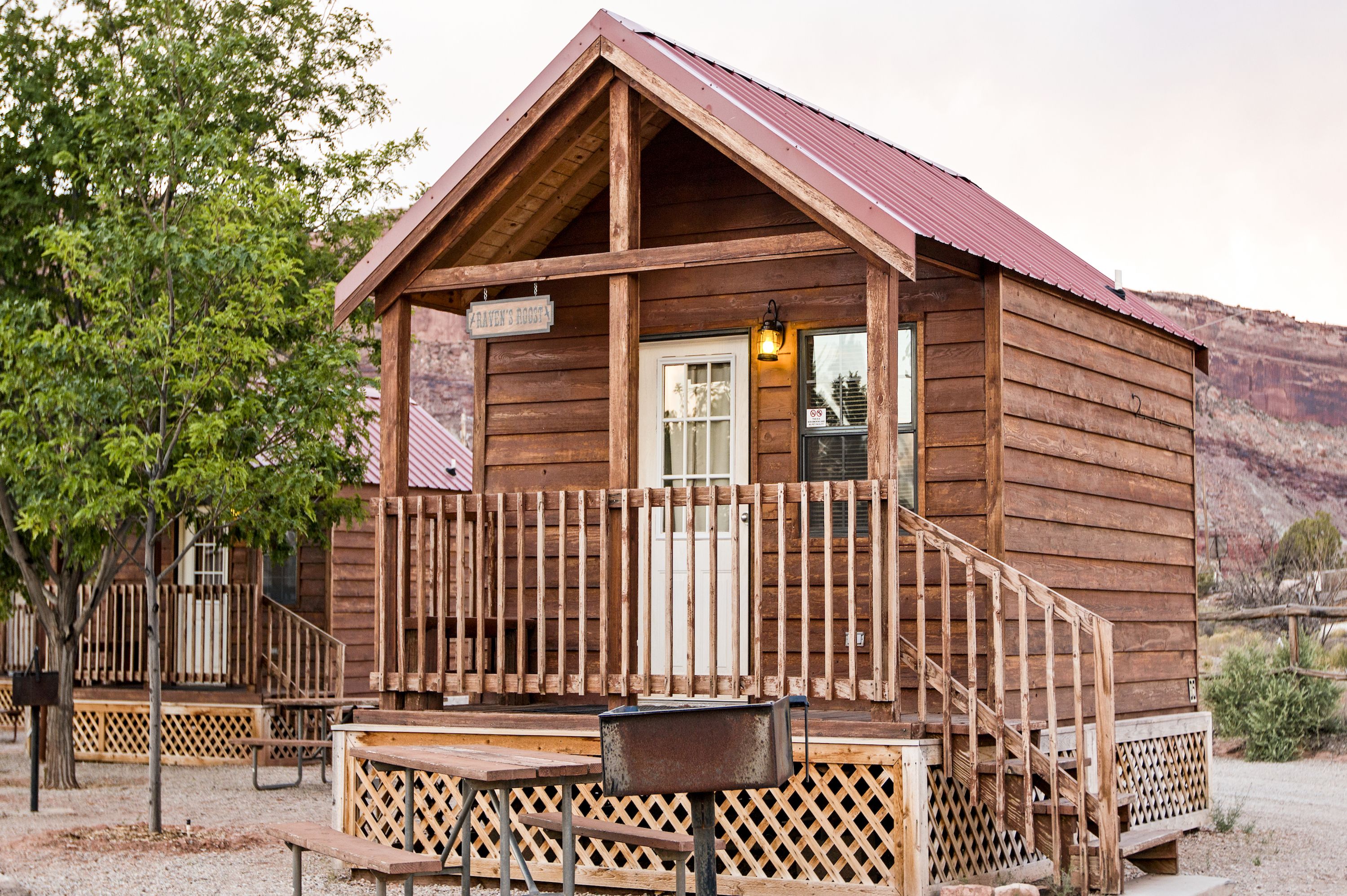 A wooden cabin with a porch, a bench, and a trash can.