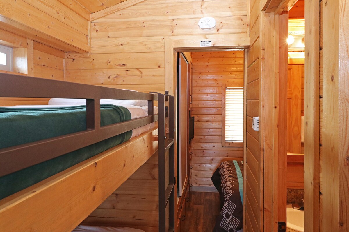 A wooden cabin with bunk beds, a small bathroom, and a visible window.