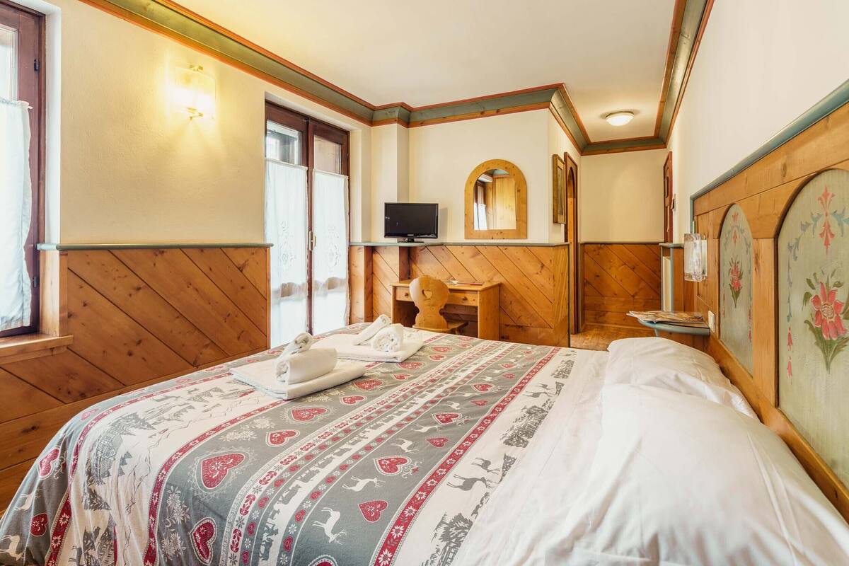 Een hotelkamer met een wand bekleed met hout, een bed met een beddekleed met dessin, een televisie, een spiegel en een klein tafeltje met handdoeken.