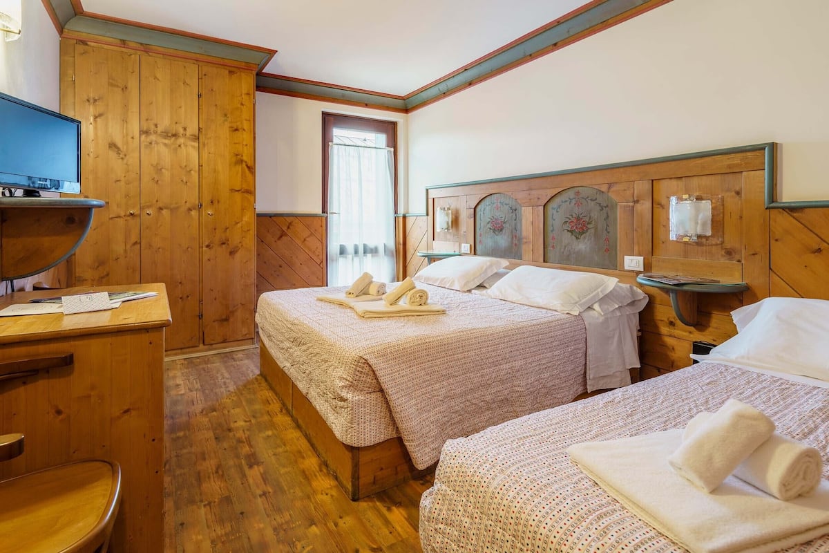 Een kamer met twee bedden, een houten garderobe, bureau met computer en televisie.