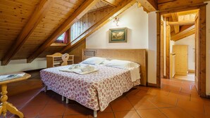 Une chambre mansardée chaleureuse avec un plafond en bois, un lit recouvert d’une literie à motifs, une petite table et un tableau encadré accroché au mur.
