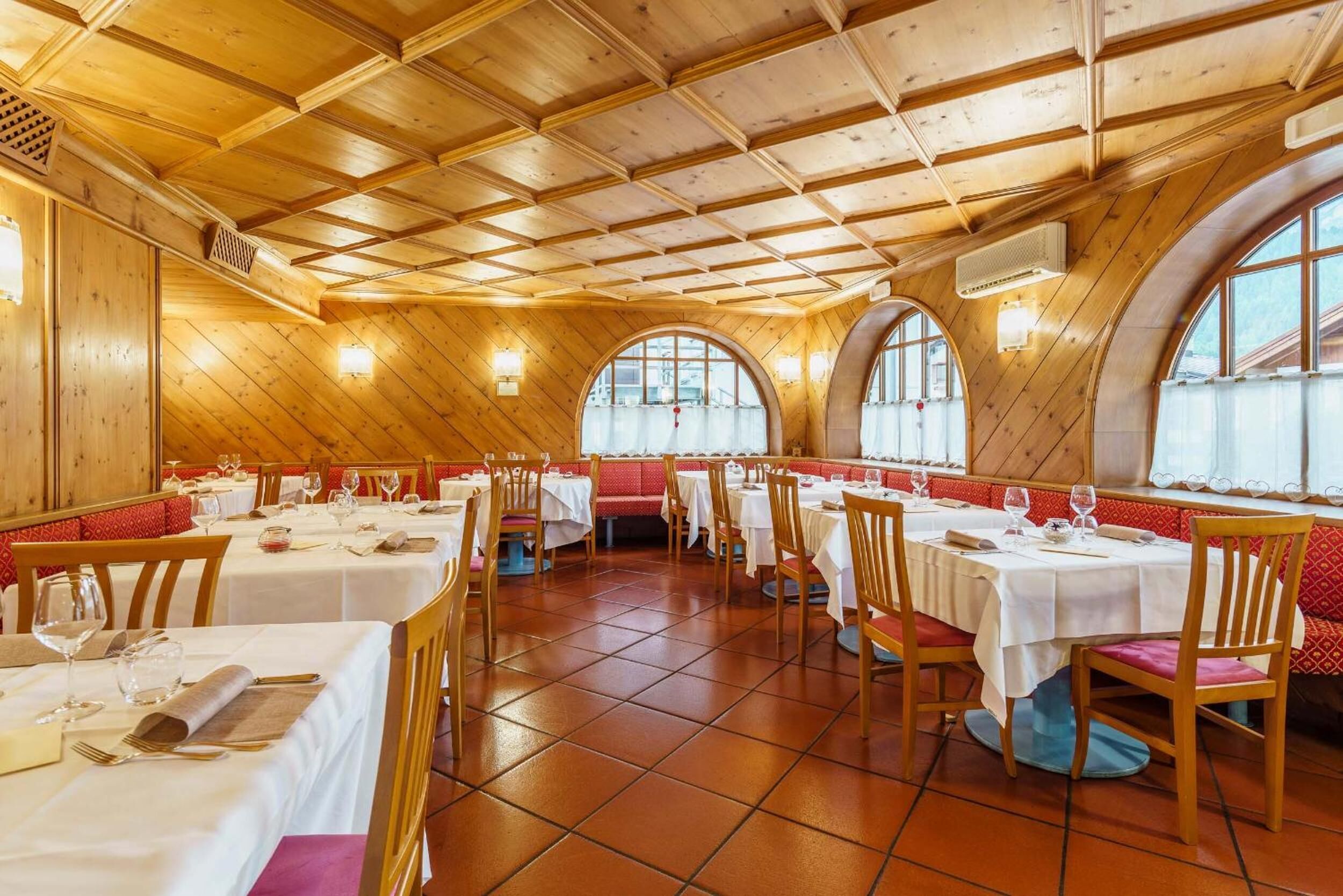 A restaurant with wooden interior, round tables, and arched windows.