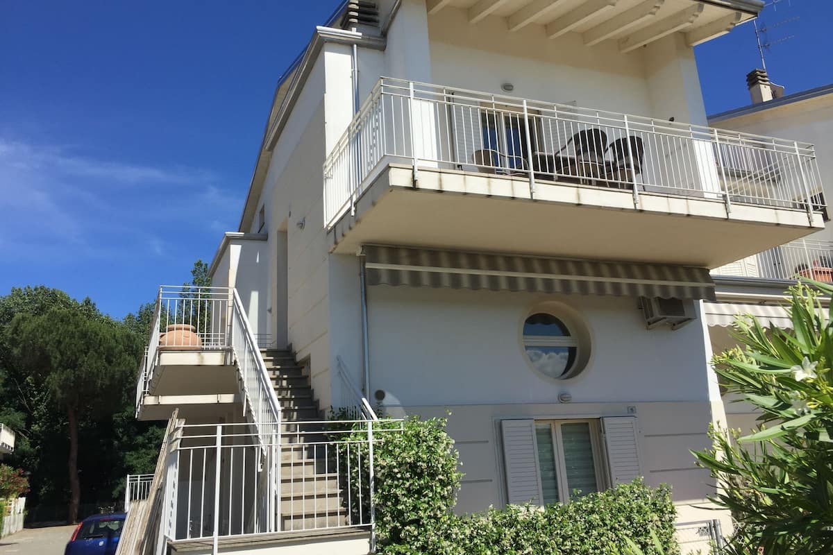 A two-story building with a balcony on the upper floor, a staircase leading to the entrance, and a round window on the facade.