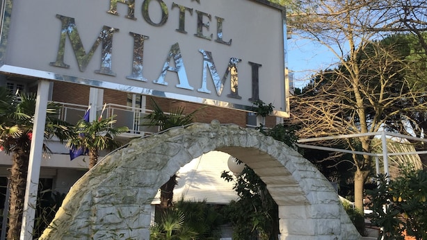 A hotel sign with "HOTEL MIAMI" written in large letters, an archway, and some greenery. - Hotel Miami (Ravenna)