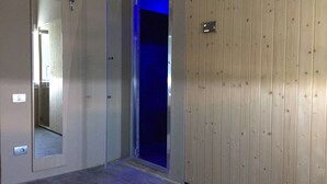 A hallway with a mirror, a door with a blue light, and a wooden panel wall. - Hotel Miami (Ravenna)