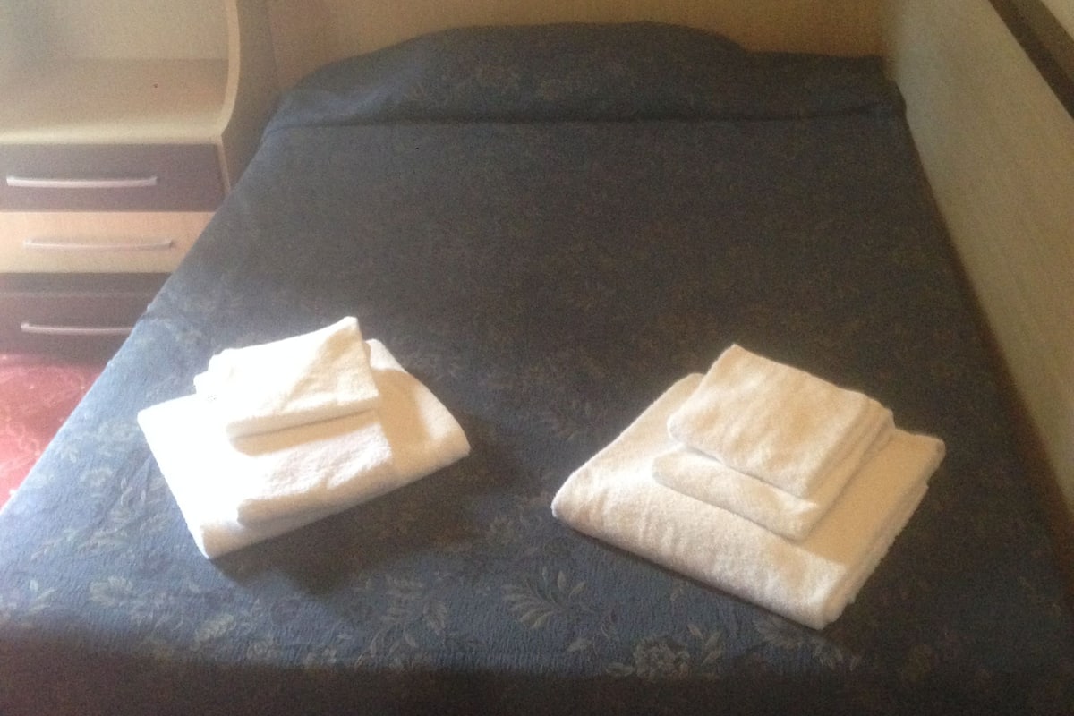 A bed with a dark blue bedspread and two neatly folded white towels on it.
