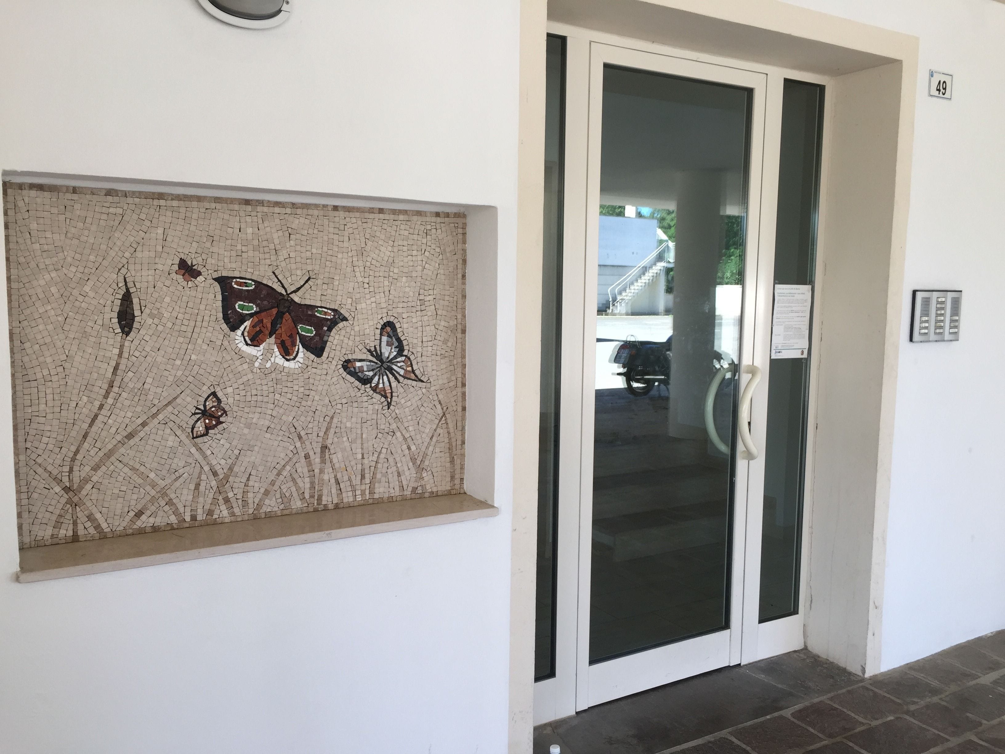 Un pasillo con un mosaico de mariposas y una puerta de cristal que da a un estacionamiento.