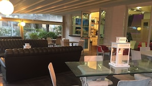 A modern interior with a glass table, white chairs, a black leather sofa, and a white lantern. - Hotel Miami (Ravenna)