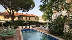 A swimming pool with lounge chairs and umbrellas, surrounded by trees and buildings. - Hotel Miami (Ravenna)