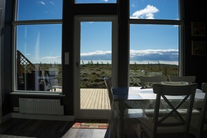 A room with a large window, a wooden deck, and a table with chairs.