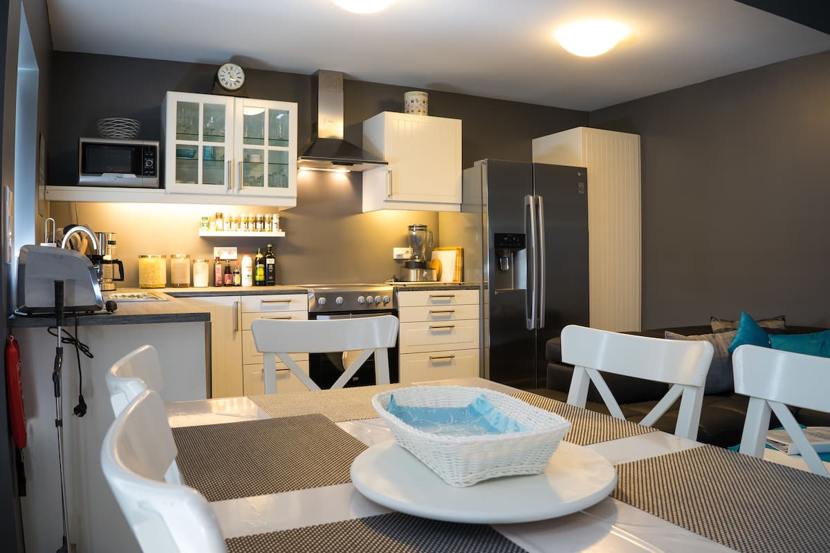 A modern kitchen with white cabinetry, a stainless steel refrigerator, and a dining area with a table and chairs.