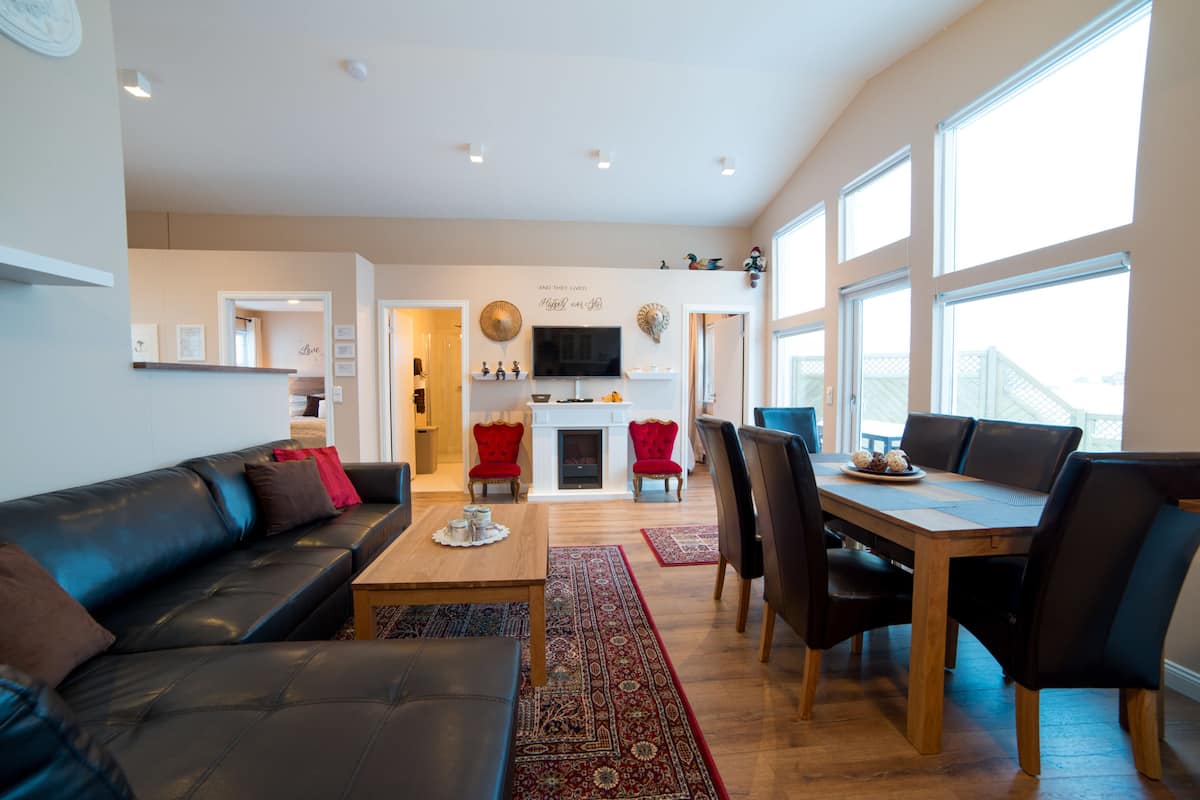 A spacious living area with a sofa, coffee table, and dining table with chairs. A fireplace is visible in the background.