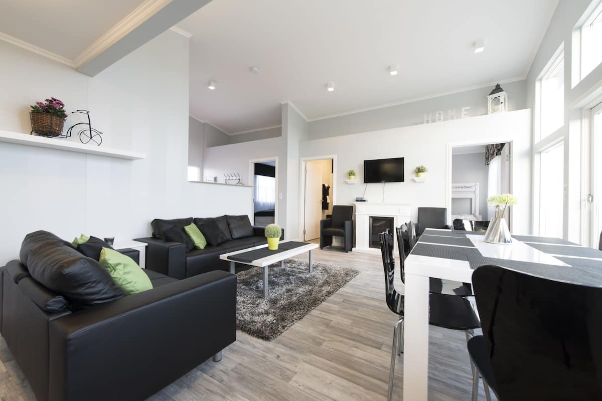 A modern living room with a sofa, coffee table, and dining area. There is a television mounted on the wall and a fireplace in the background.