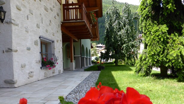 Ein Steinhaus mit Balkon, ein Garten mit roten Blumen und ein Baum.
