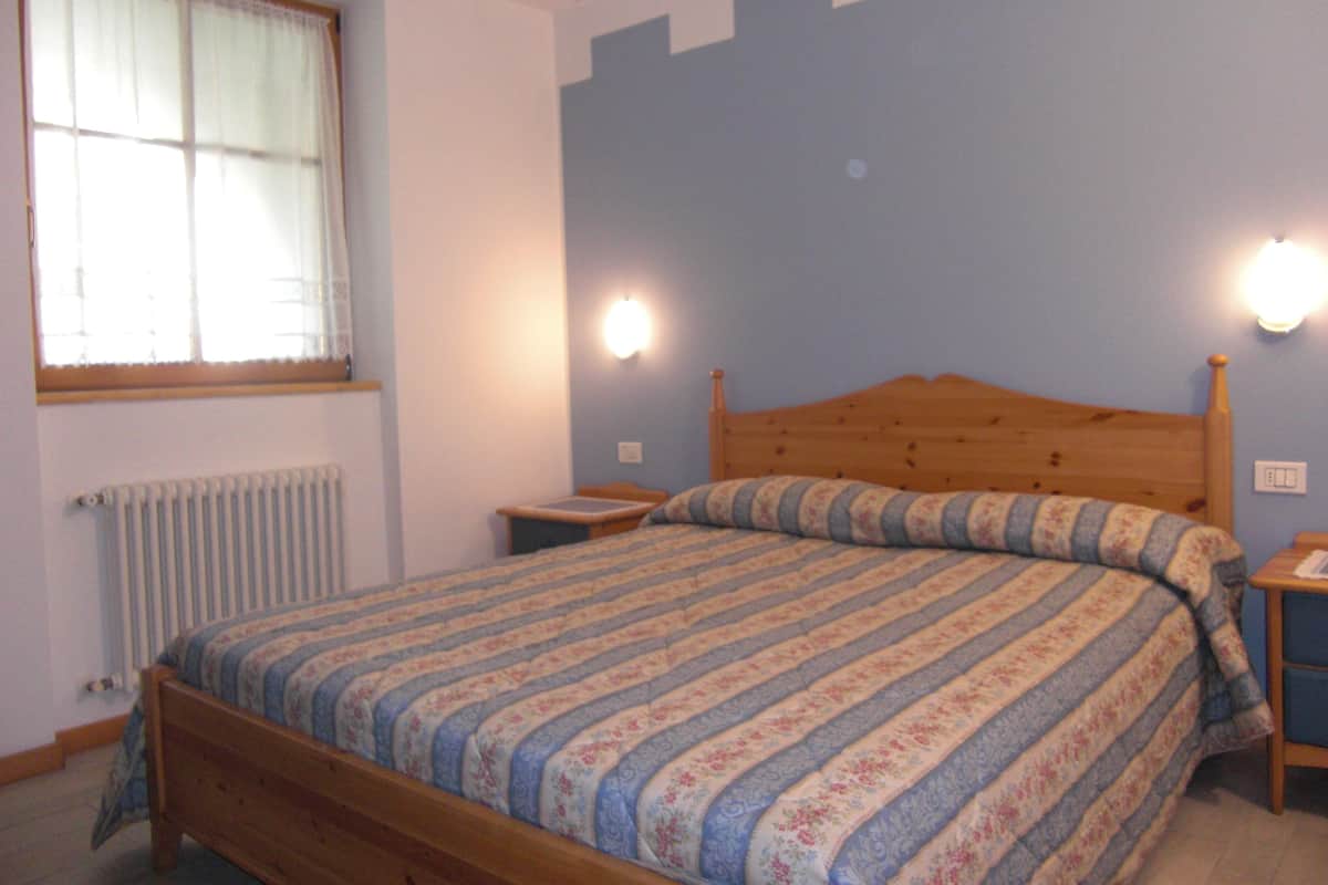 A bedroom with a wooden bed, a window with curtains, and two wall-mounted nightstands.