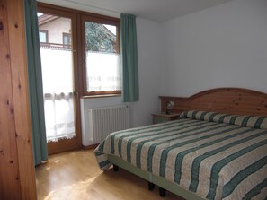 Un dormitorio con una cama de madera, una mesita de noche, una ventana con cortinas y un radiador.