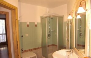 Un baño con ducha envuelta en vidrio, un lavamanos y un espejo.