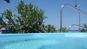 Una piscina azul cristalina con una escalera metálica y una barandilla de metal.