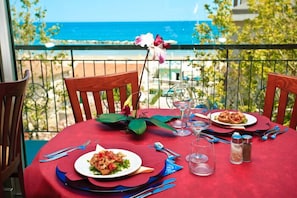 A table set for two with plates of food, cutlery, and glasses on a red tablecloth, overlooking a coastal view.