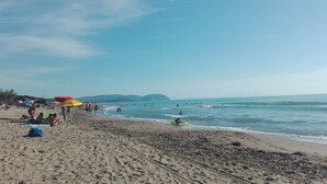 Una playa con gente tomando el sol y nadando, sombrillas y un cielo despejado.