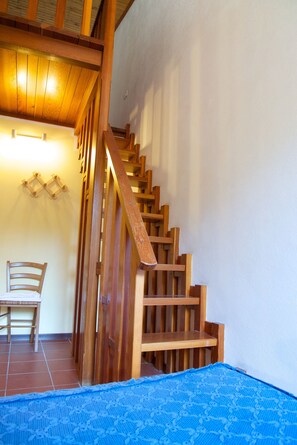Una escalera de madera con barandilla, una silla de madera y una alfombra azul estampada en el suelo.