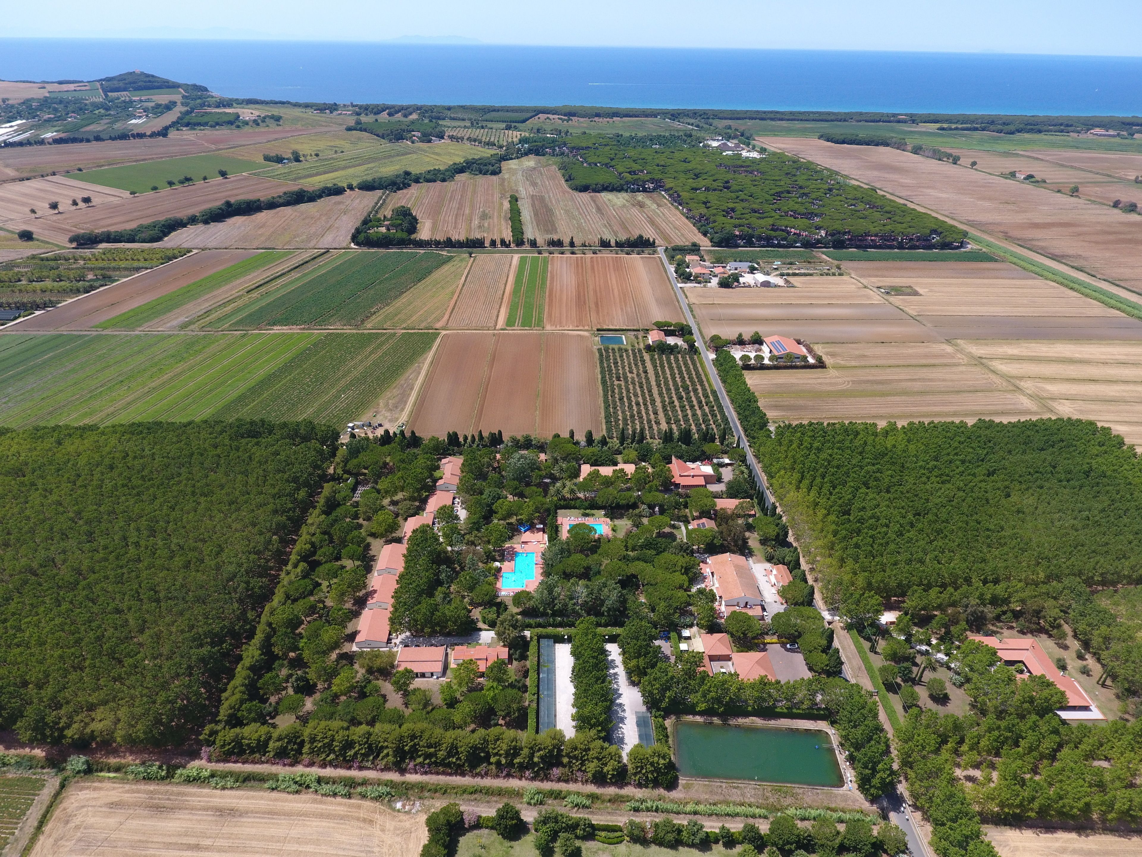 Luchtbeeld van een landelijk gelegen pand met velden, een zwembad en een klein huis omringd door bomen.