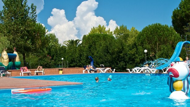 Una piscina con agua cristalina azul, rodeada de sillas de descanso y un tobogán.