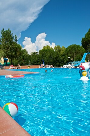 Una piscina con agua cristalina azul, rodeada de sillas de descanso y un tobogán.