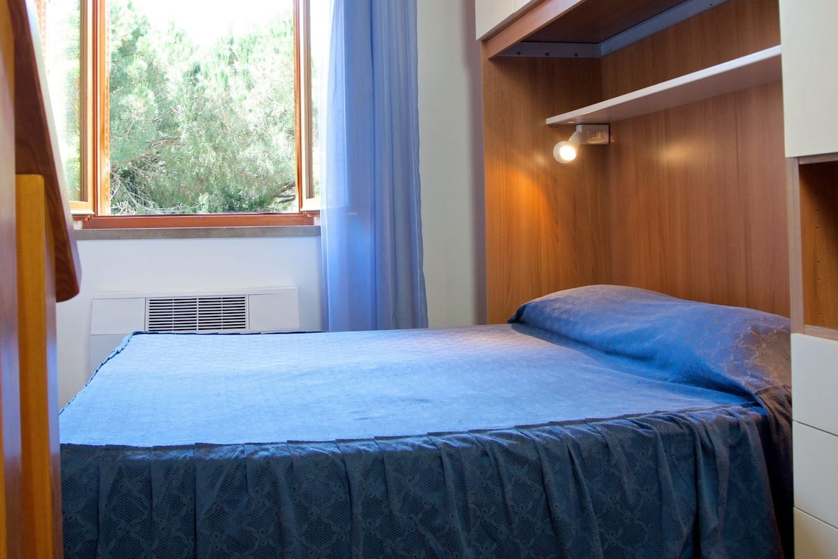 Un dormitorio con cama, ventana con cortinas, armario empotrado y techo inclinado.