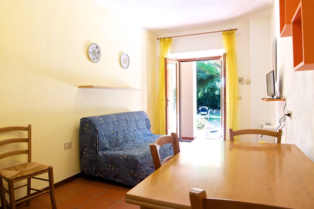 Un comedor con una mesa y sillas de madera, un sofá azul cubierto y vistas a un área exterior a través de una puerta.