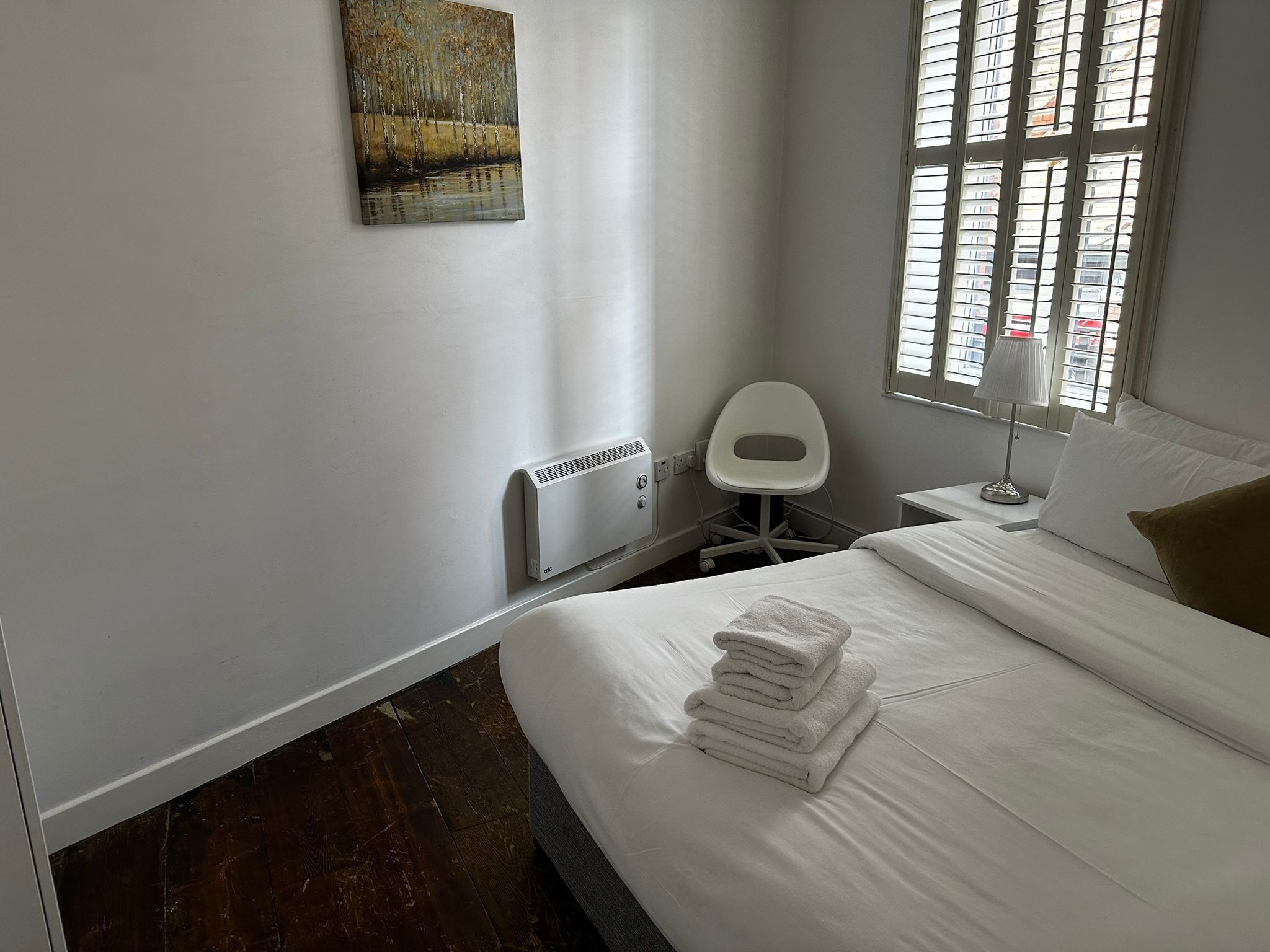 Ein Hotelzimmer mit Bett, Sessel, Heizkörper, einem Fenster mit Jalousien und einem Bild an der Wand.