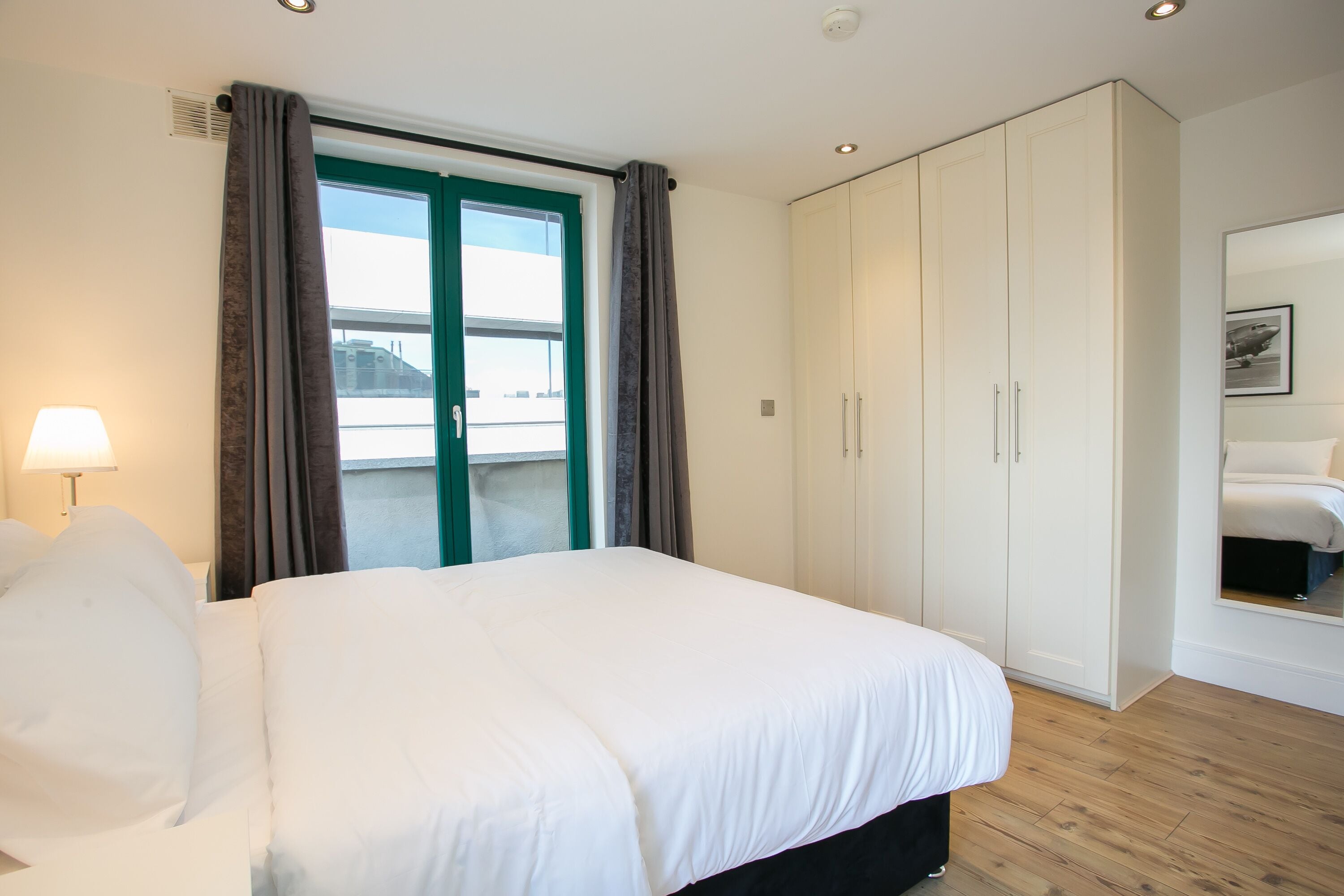 A hotel room with a bed, a wardrobe, a window with curtains, and a lamp.