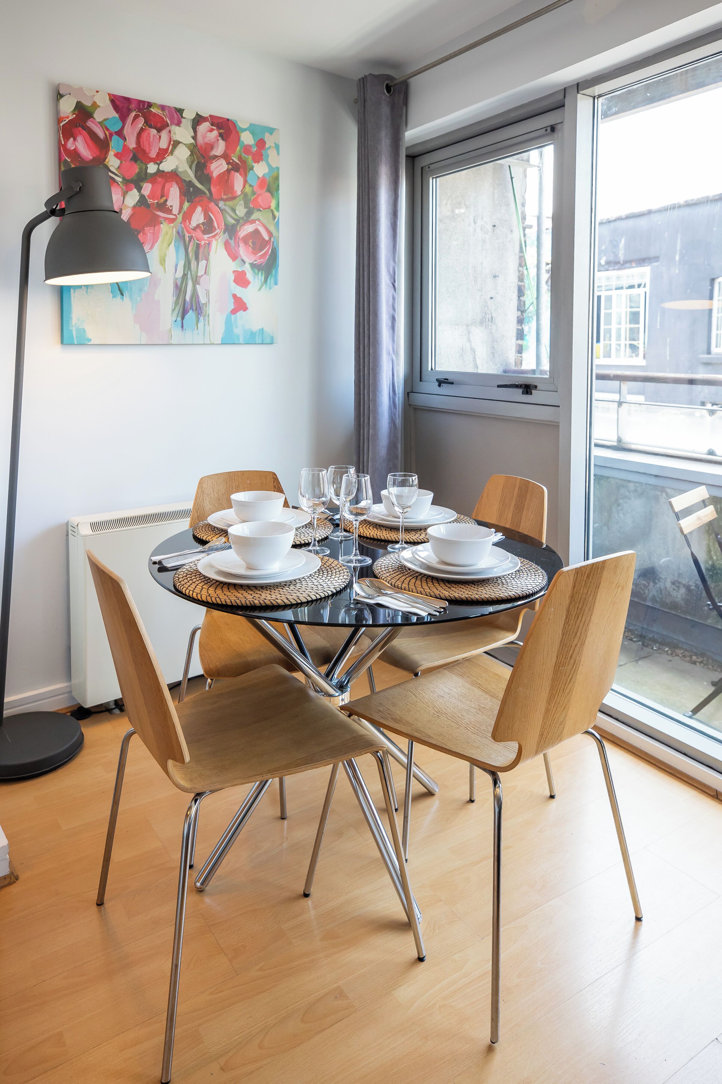 A dining area with a round table set for four, surrounded by wooden chairs with metal legs.