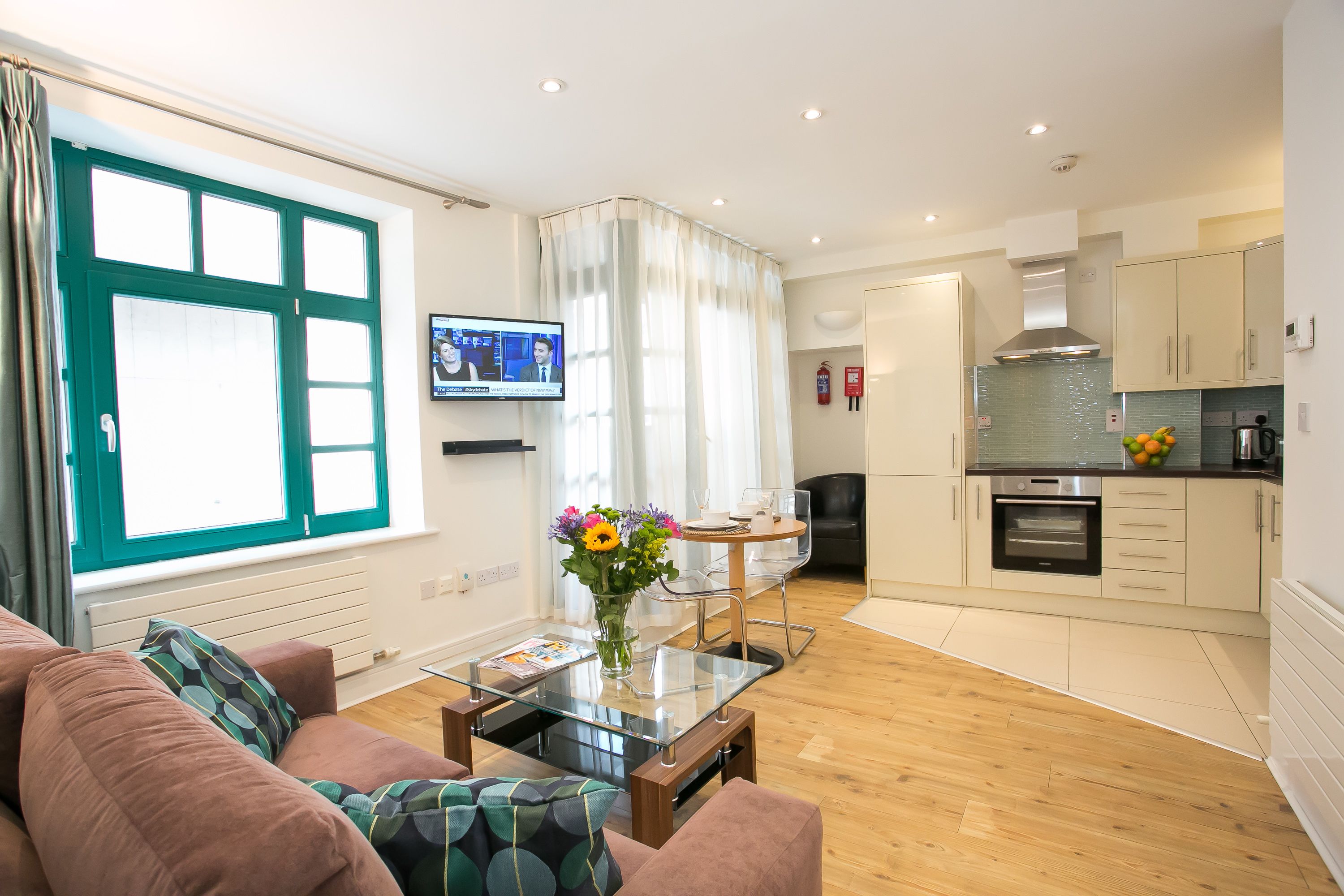 A modern living room with a sofa, a glass coffee table, and a TV mounted on the wall.