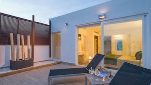 Un espace extérieur moderne, aménagé avec des fauteuils confortables et une porte vitrée donnant sur un intérieur bien éclairé.
