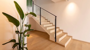 Un escalier moderne avec des rampes en verre et des marches en bois, menant à l’étage supérieur.