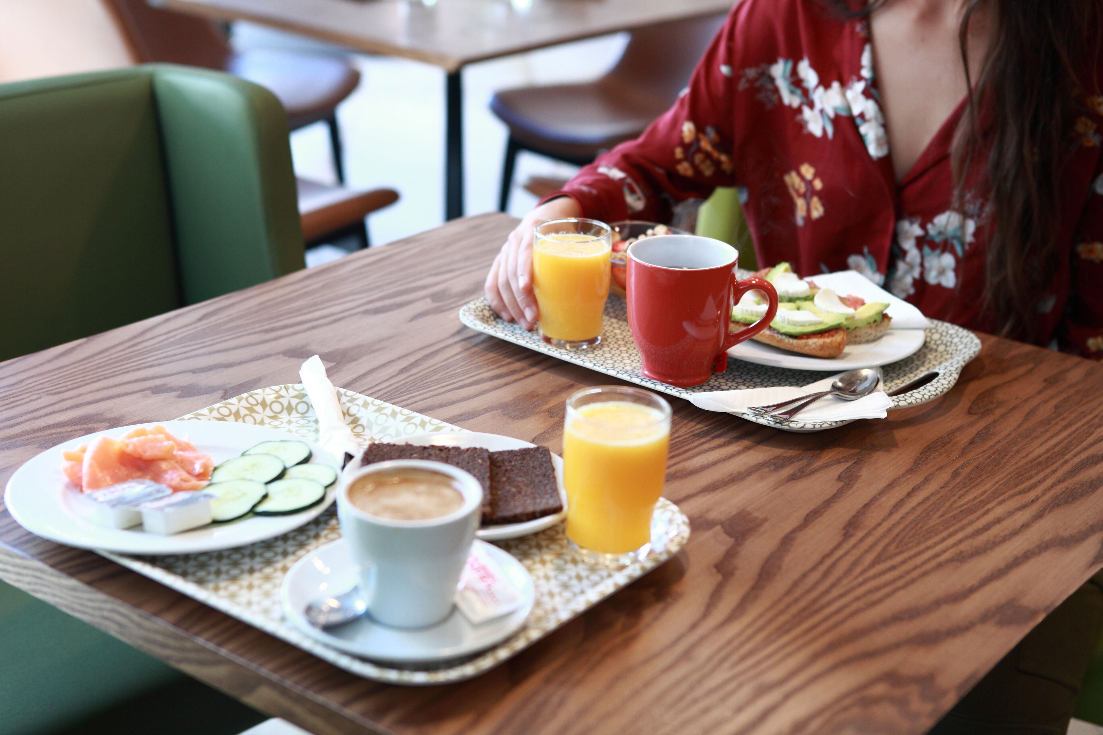 Bandeja de desayuno con salmón ahumado, rodajas de pepino, una taza de café y un vaso de jugo de naranja sobre una mesa de madera.
