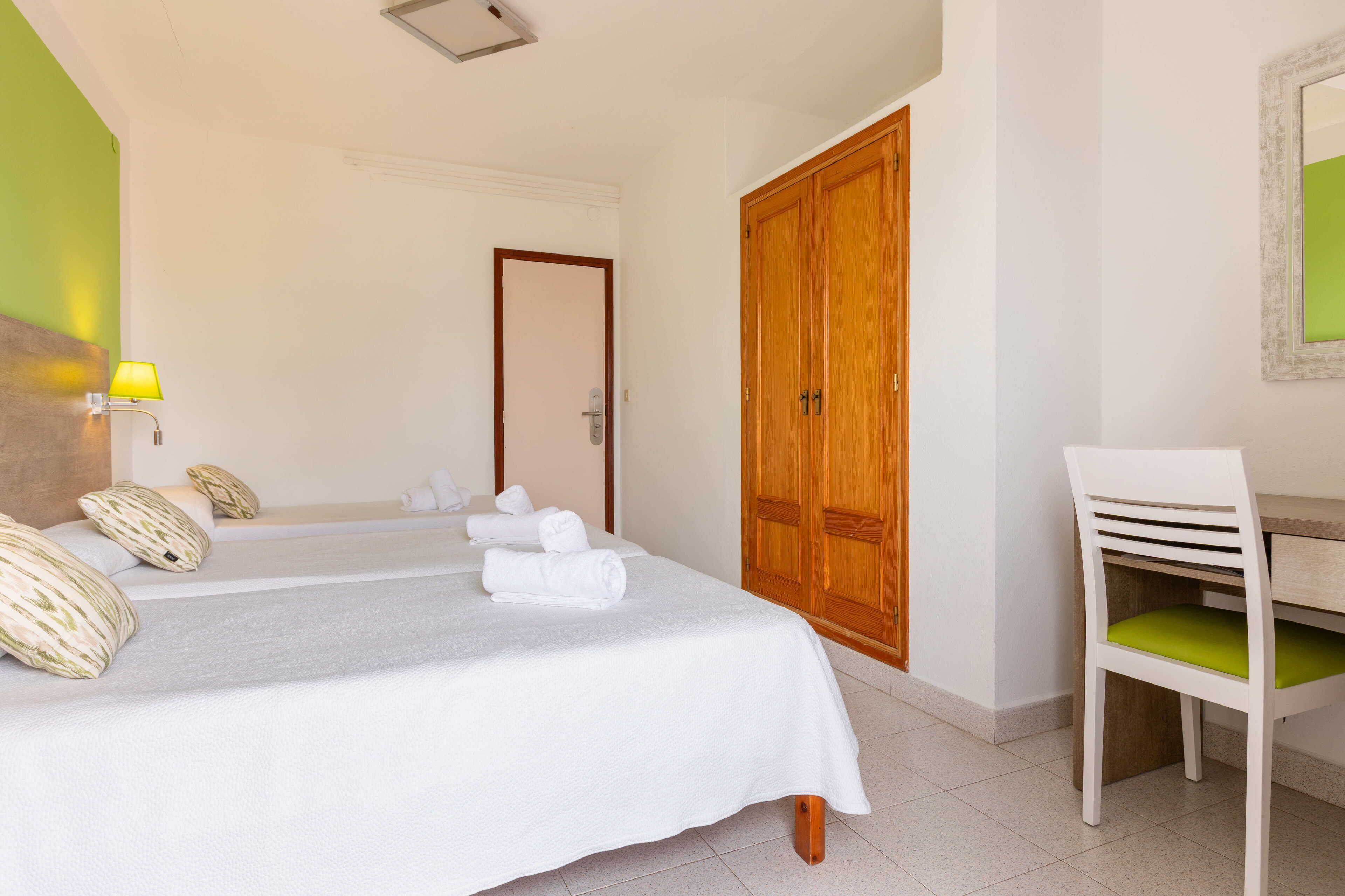 A hotel room with a bed, a desk, a chair, and a wardrobe.