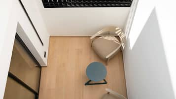 Una habitación moderna con piso de madera, dos sillas color beige, una mesita redonda y una ventana con persianas.