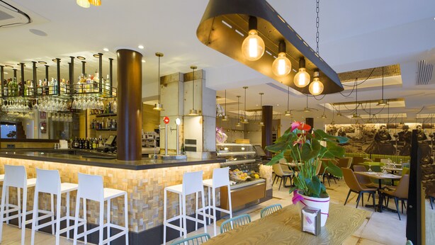 Un espace bar moderne avec un comptoir en bois, des tabourets de bar blancs et des luminaires suspendus.