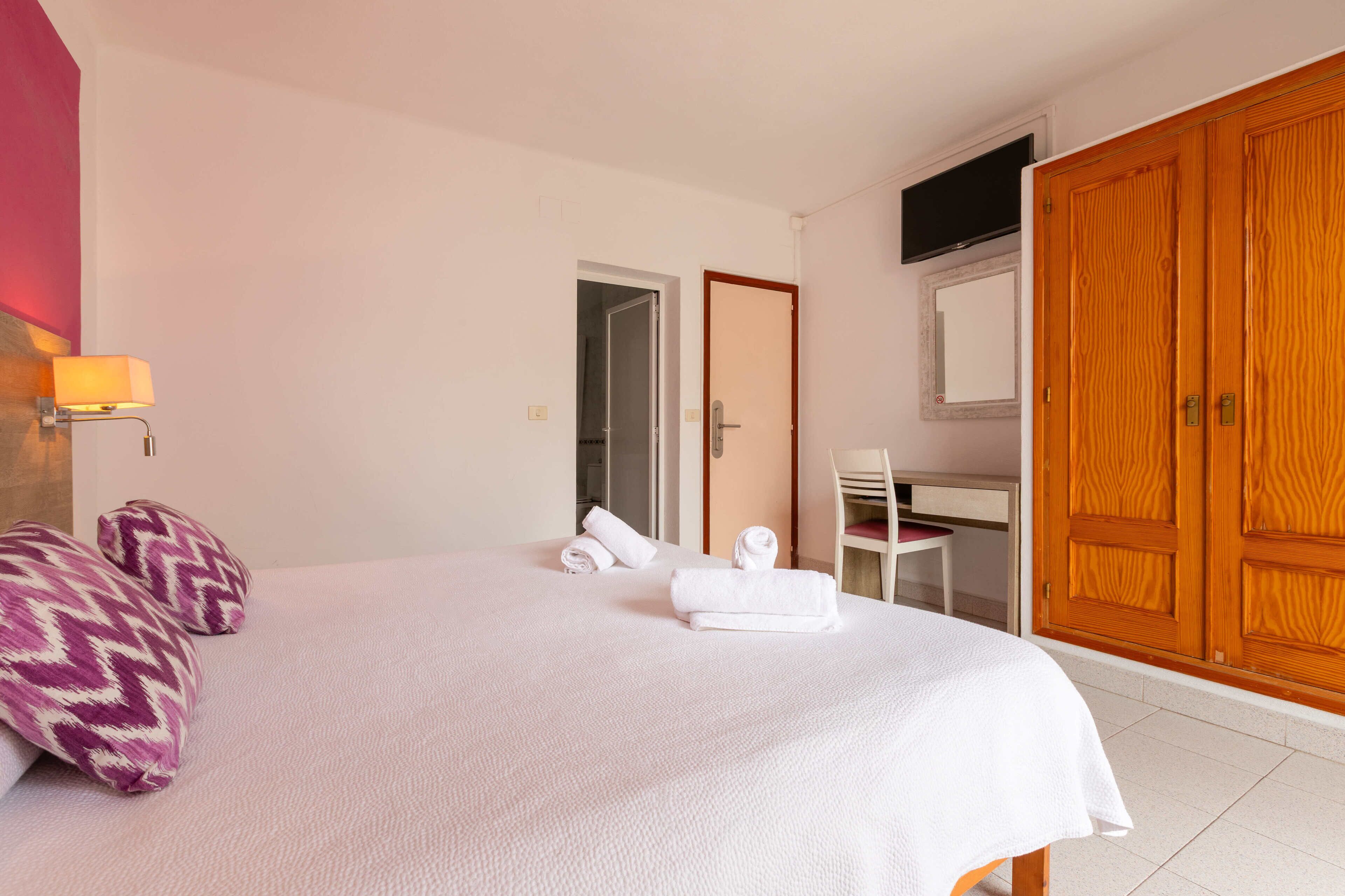 A hotel room with a bed, a desk, a chair, and a wardrobe.