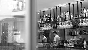 Un espace bar avec des étagères remplies de bouteilles d’alcool et des verres à vin suspendus.