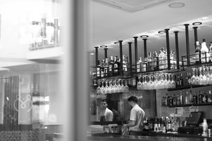 Zona de bar con estantes llenos de botellas de licores y copas de vino colgando.