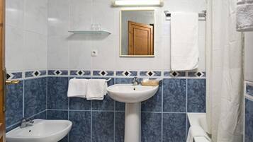 A bathroom with a pedestal sink, a bidet, a mirror, and a shower curtain.