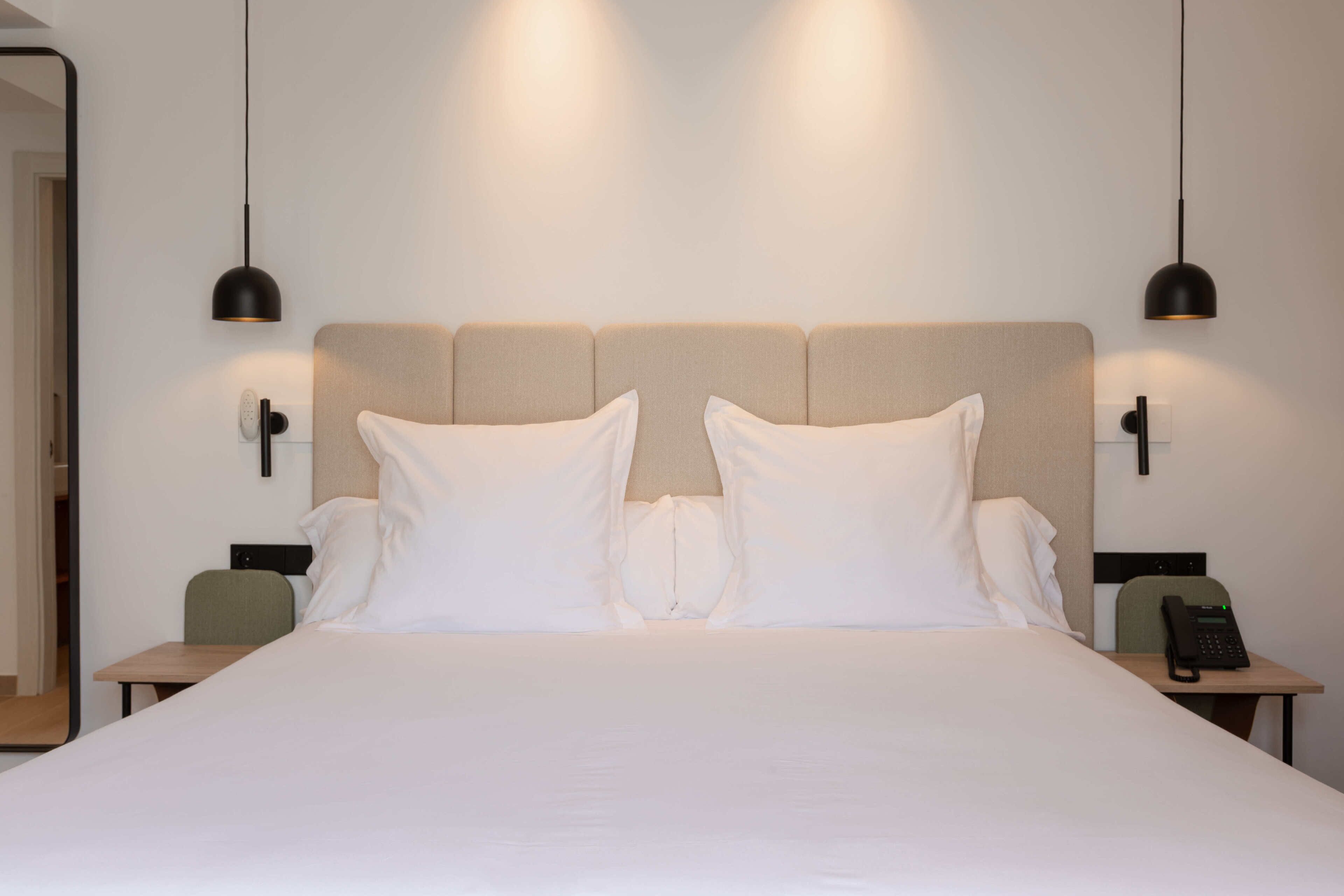 A neatly made bed with white linens, two bedside tables with lamps, and a telephone on one of the tables.
