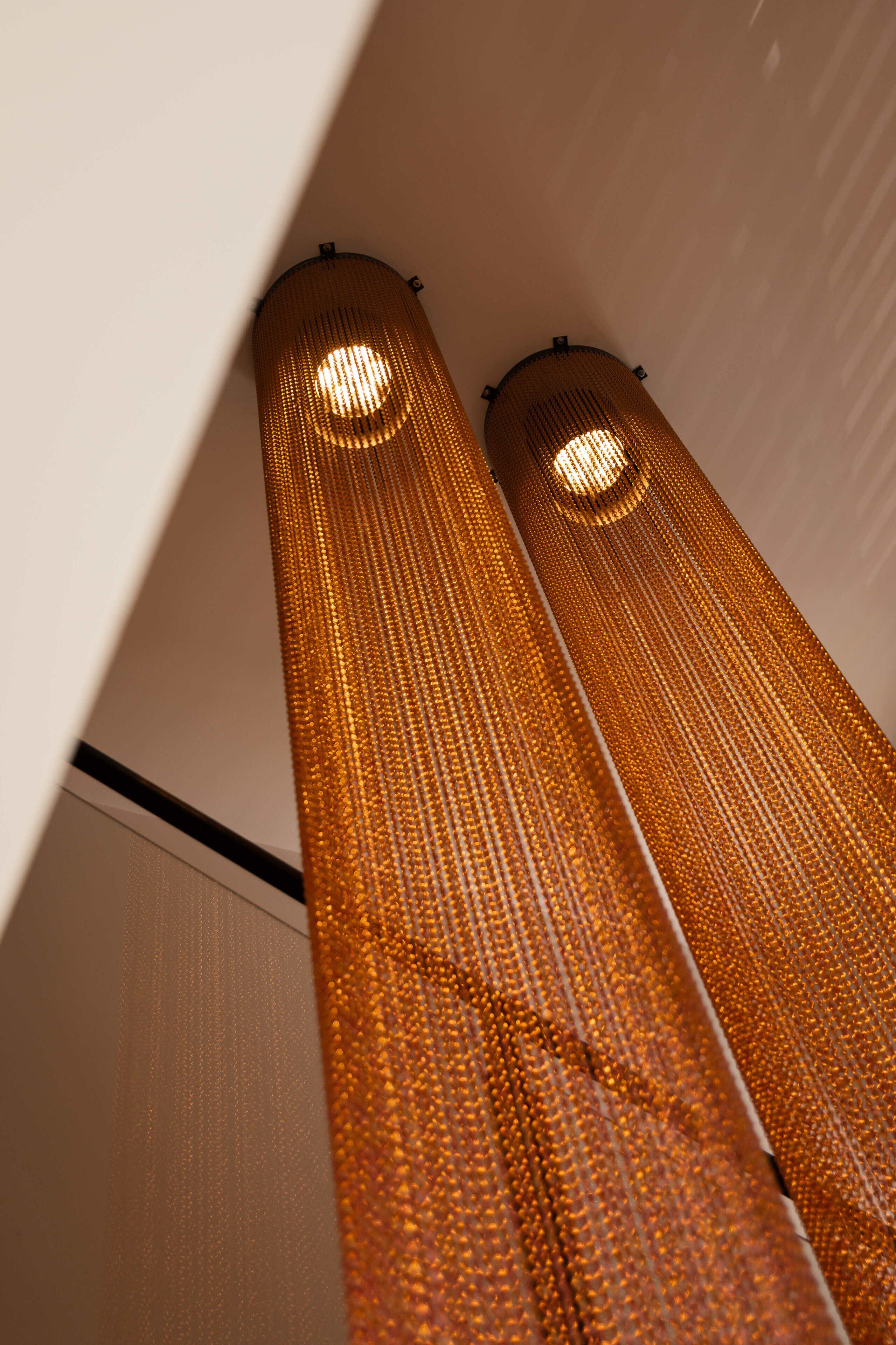 Deux luminaires cylindriques et élancés, dotés d’une surface texturée et de sources de lumière circulaires situées en partie supérieure.