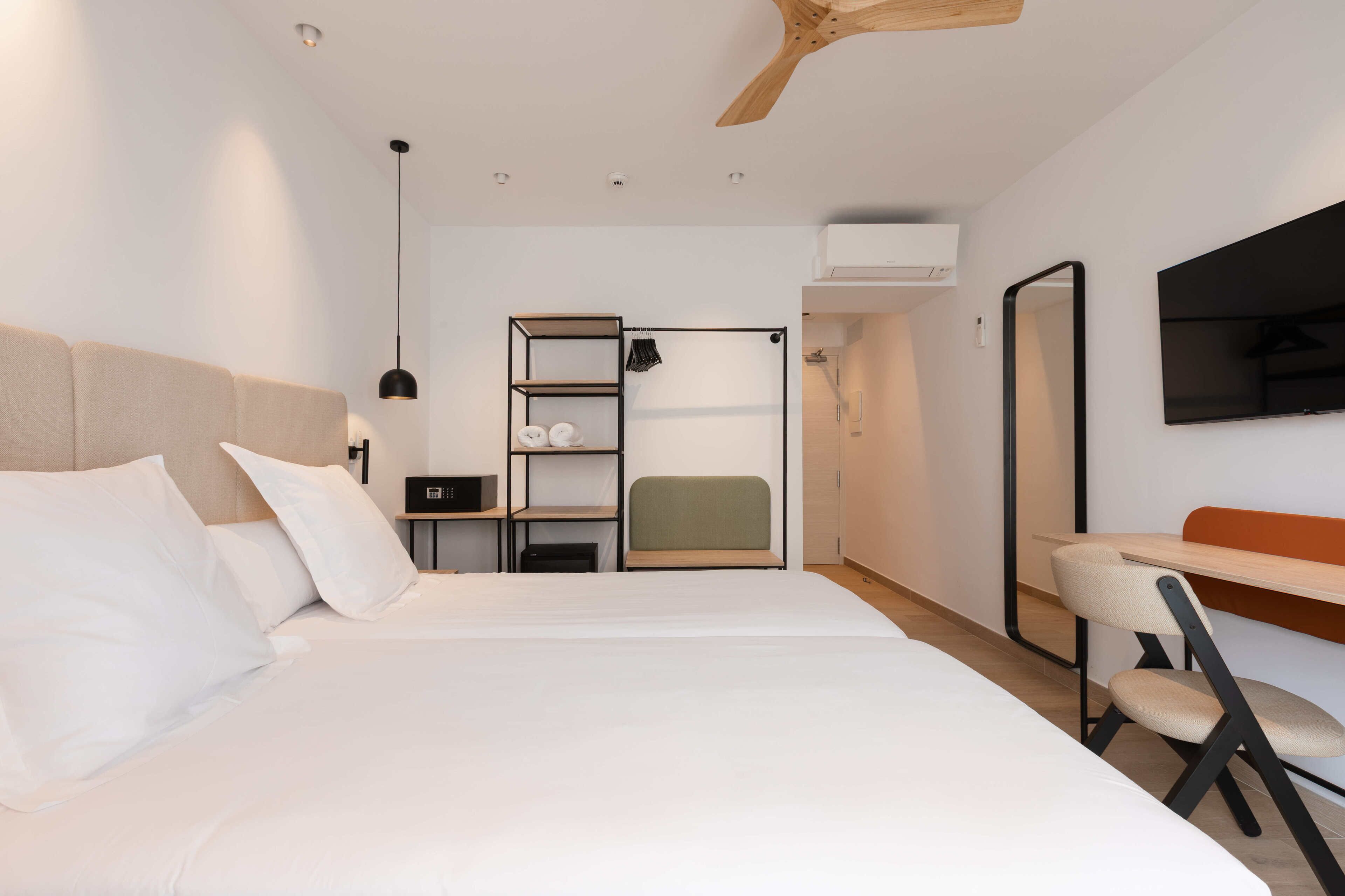 A modern hotel room with a large bed, a desk, a chair, a TV, and a wardrobe.