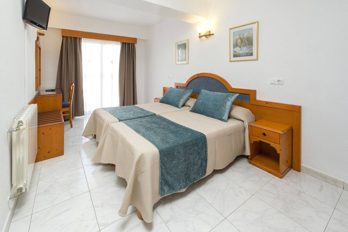 Ein Hotelzimmer mit Bett, Nachttischen, Schreibtisch, Stuhl, Fernseher und Heizkörper.