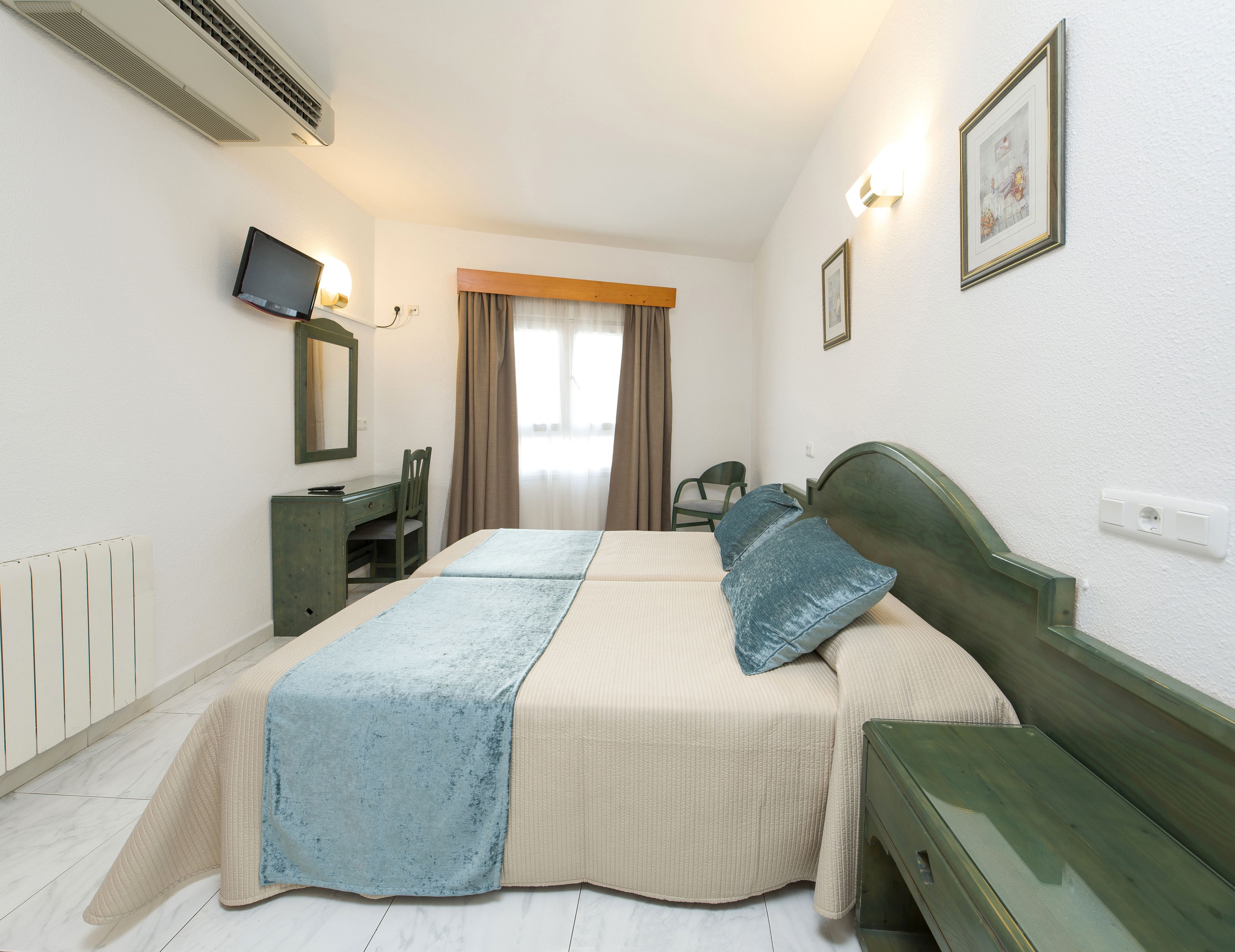Habitación de hotel con cama, escritorio, silla, televisor y ventana con cortinas.
